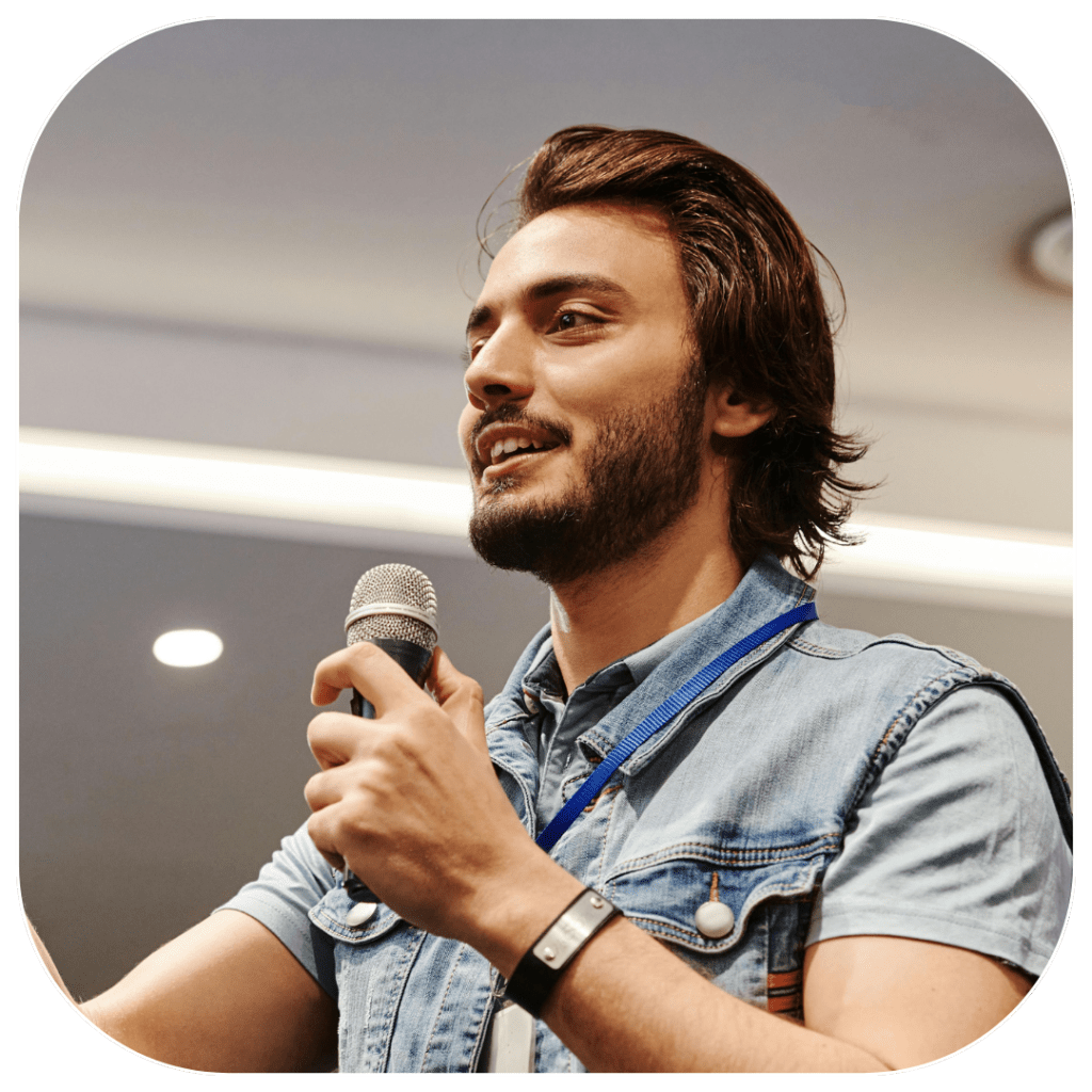 Young man holding microphone and giving a talk on a stage in English